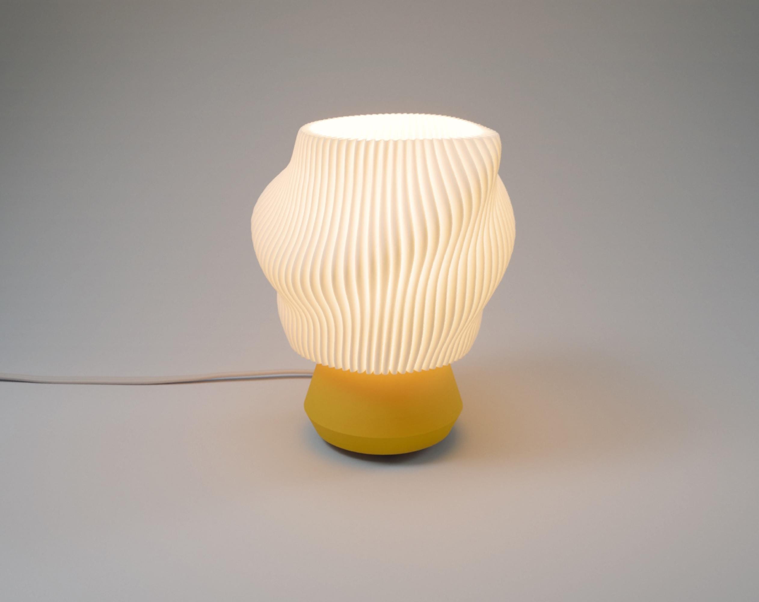 Illuminated wavy pleated white lamp with a yellow base photographed in a studio