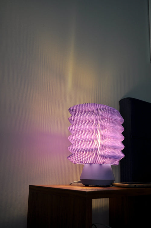 Lavender Bellows Weave Lamp illuminated on a nightstand