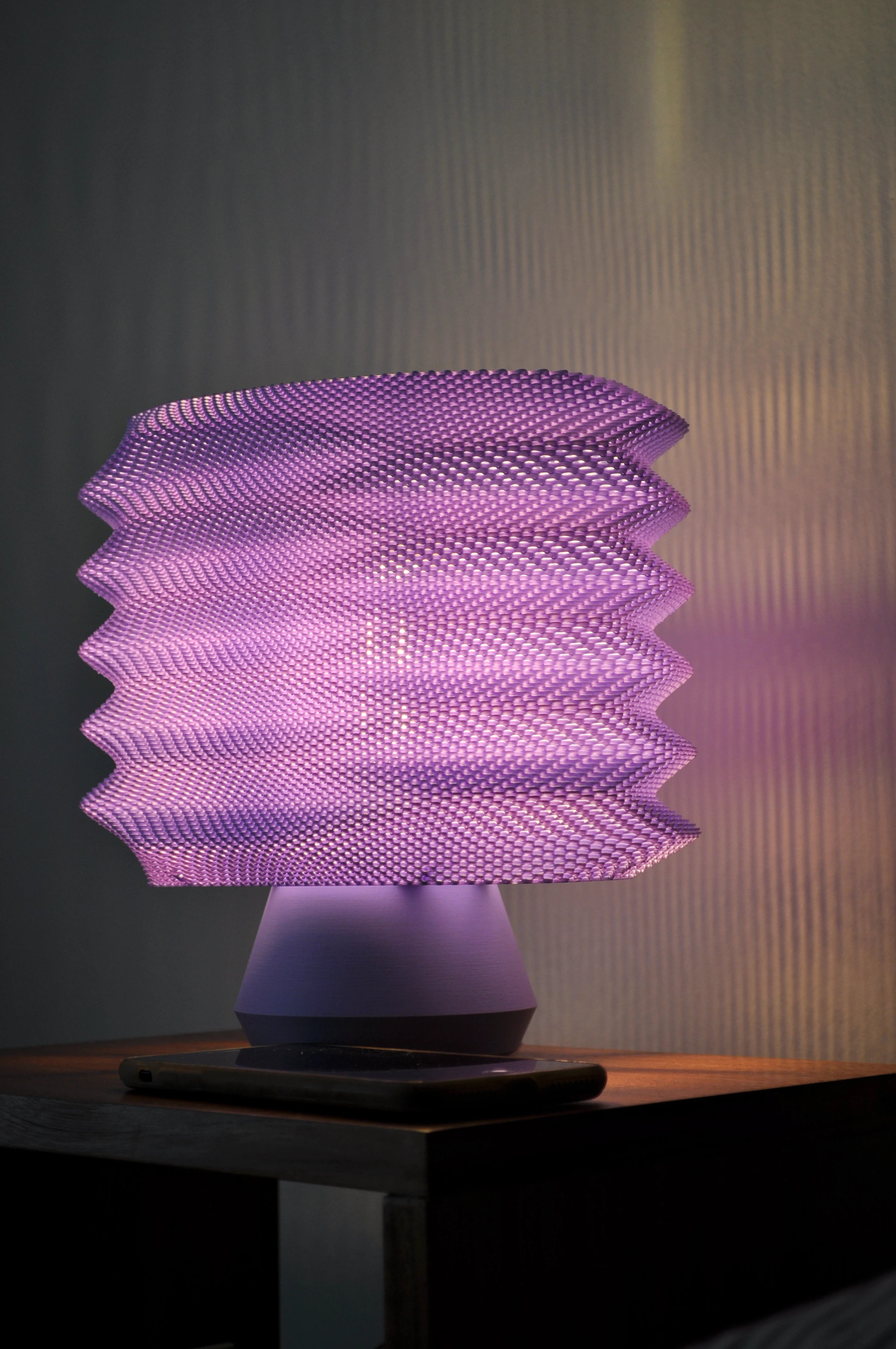 Lavender Bellows Weave Lamp illuminated on a nightstand
