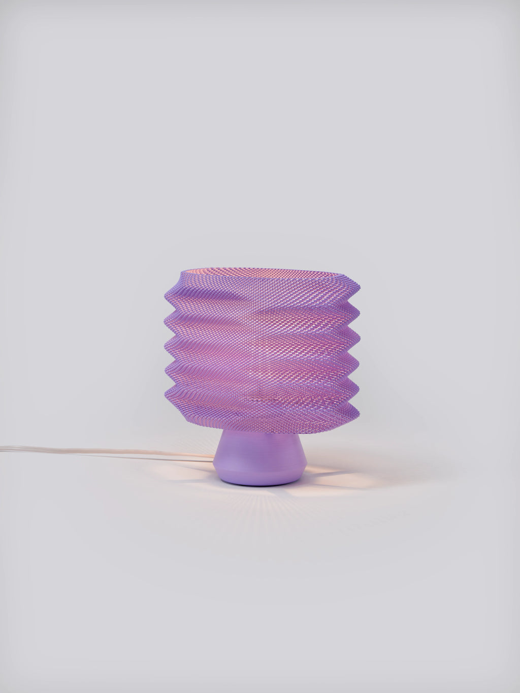 Lavender Bellows Weave Lamp illuminated on a white studio background, showing geometric shade and soft glow
