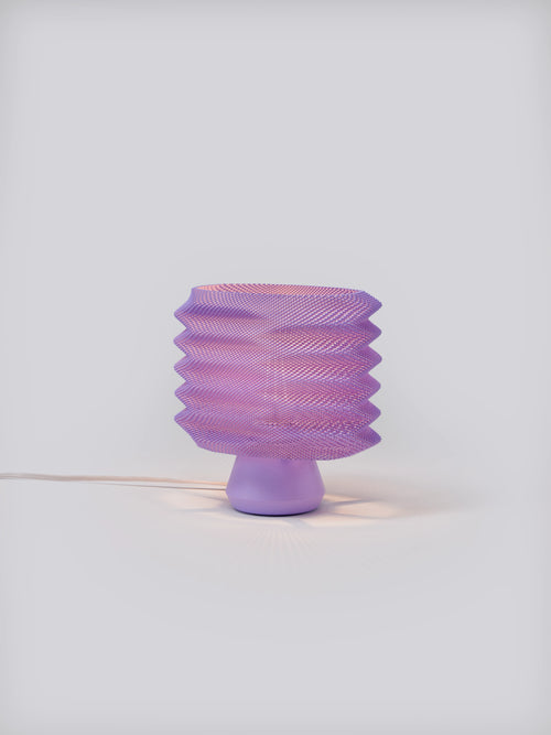 Lavender Bellows Weave Lamp illuminated on a white studio background, showing geometric shade and soft glow