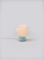 Light blue Dollop Lamp illuminated on a white studio background, showing pleated shade and soft glow