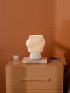 White Dollop Lamp on a wood nightstand, lit, styled with books and a terrazzo block