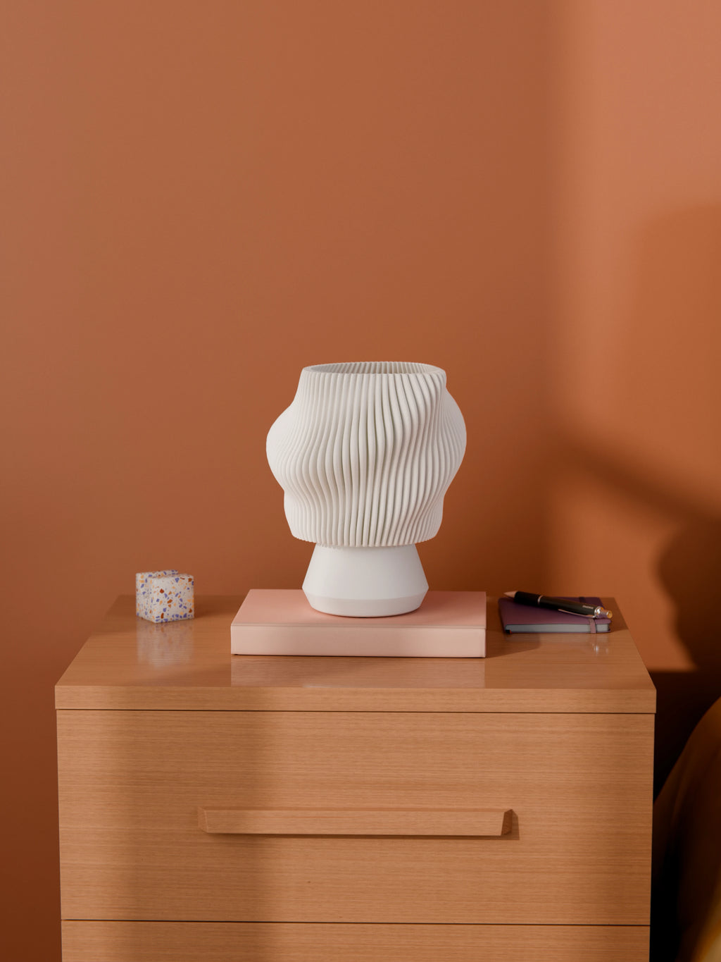 White Dollop Lamp on a wood nightstand, unlit, styled with books and a terrazzo block