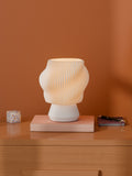 White Dollop Lamp on a wood nightstand, lit, styled with books and a terrazzo block