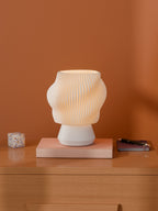 White Dollop Lamp on a wood nightstand, lit, styled with books and a terrazzo block