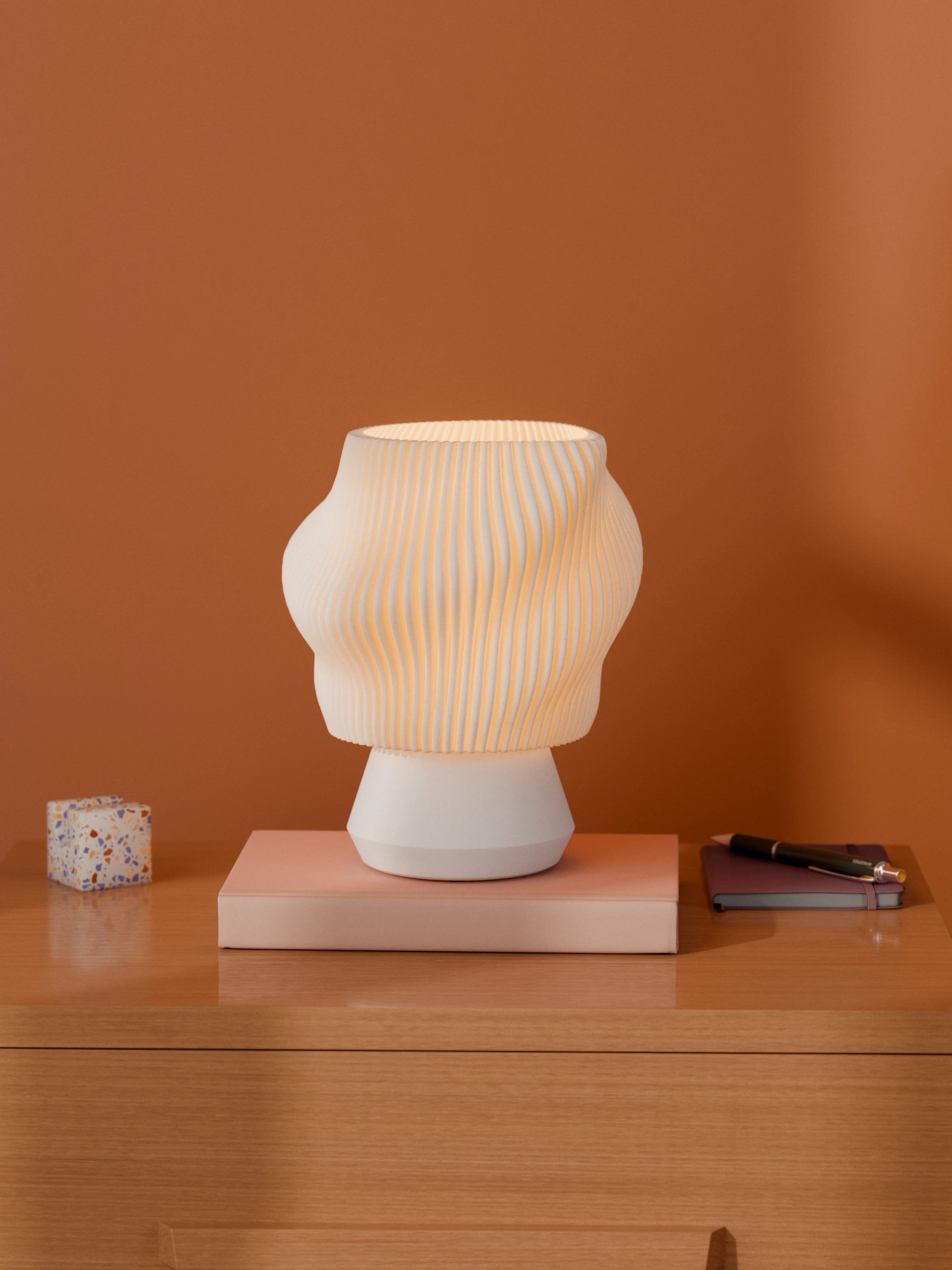 White Dollop Lamp on a wood nightstand, lit, styled with books and a terrazzo block