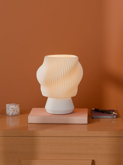 White Dollop Lamp on a wood nightstand, lit, styled with books and a terrazzo block