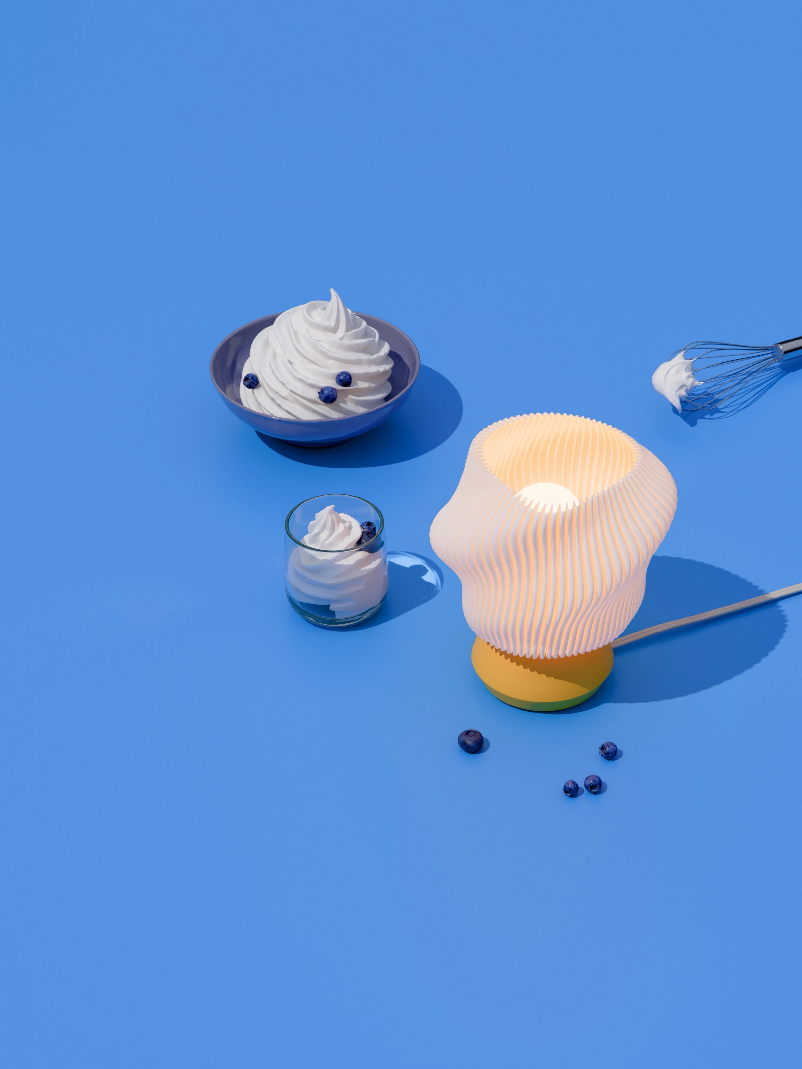 Yellow Dollop lamp illuminated on a blue surface with whip cream and blueberries.