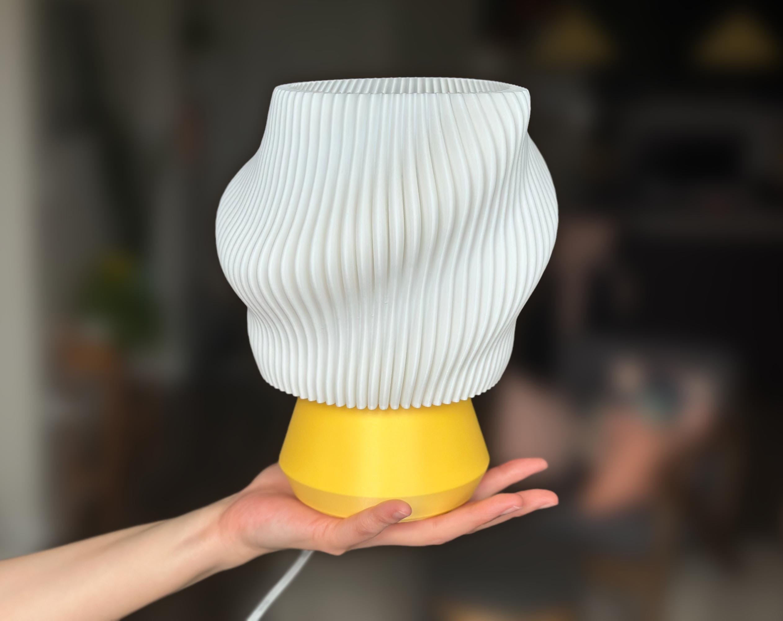 Wavy pleated white lamp with a yellow base held in a hand