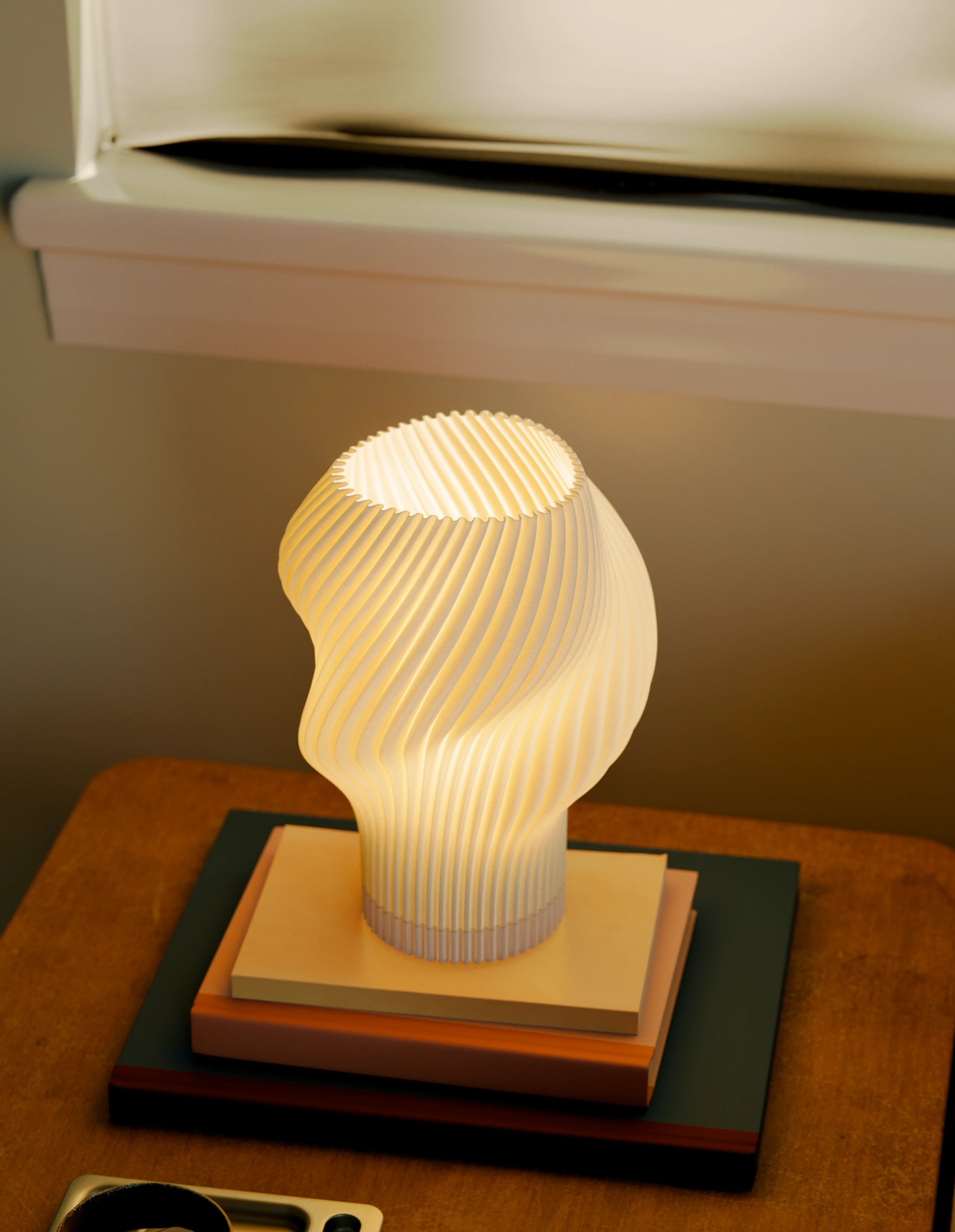 Flourish Lamp illuminated on a side table, styled with stacked books, a coffee cup, and glasses