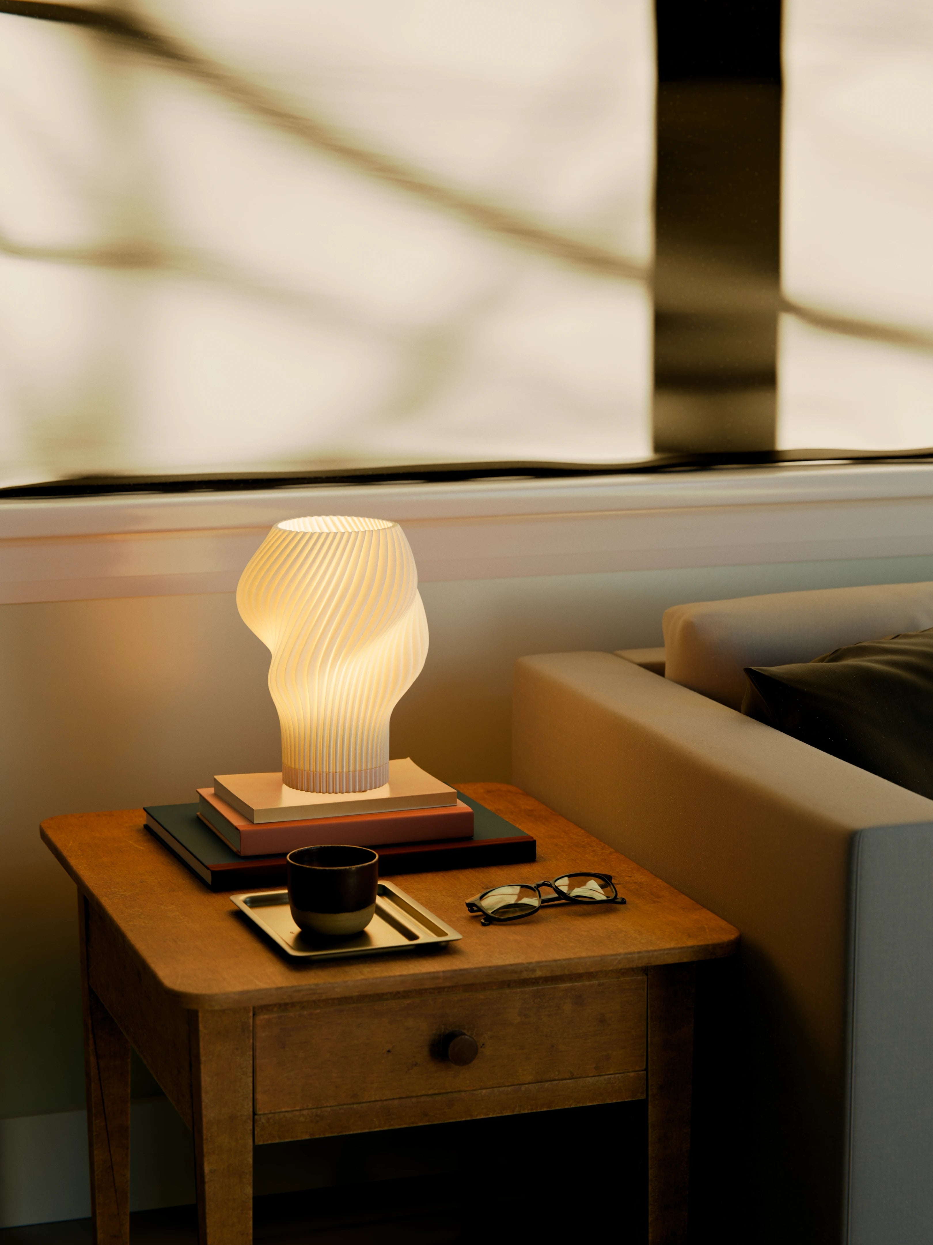 Flourish Lamp illuminated on a side table, styled with stacked books, a coffee cup, and glasses