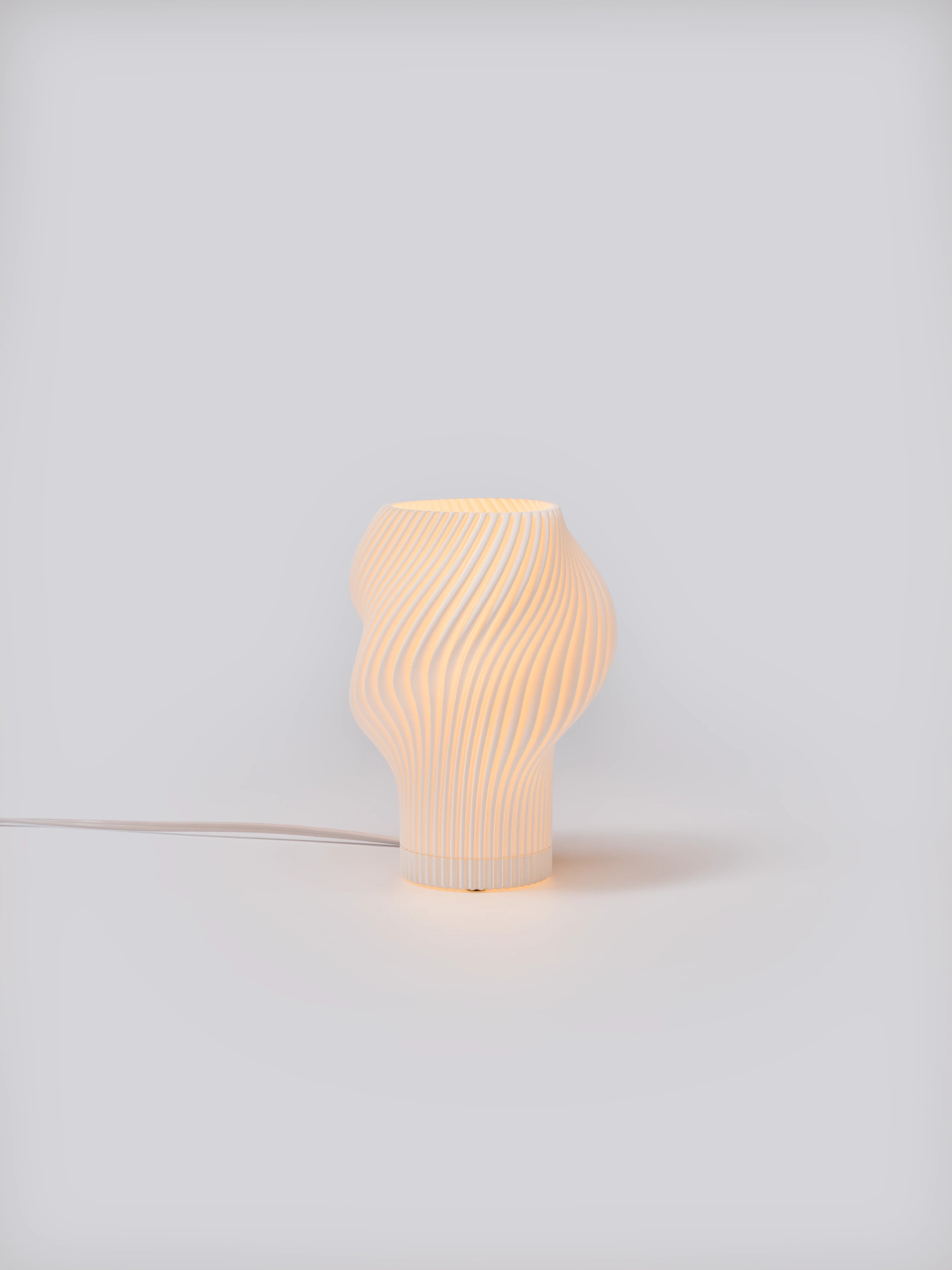 Flourish Lamp illuminated on a white studio background, showing pleated shade and soft glow