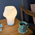 Flourish lamp illuminated on a side table with iced tea and stacked books.