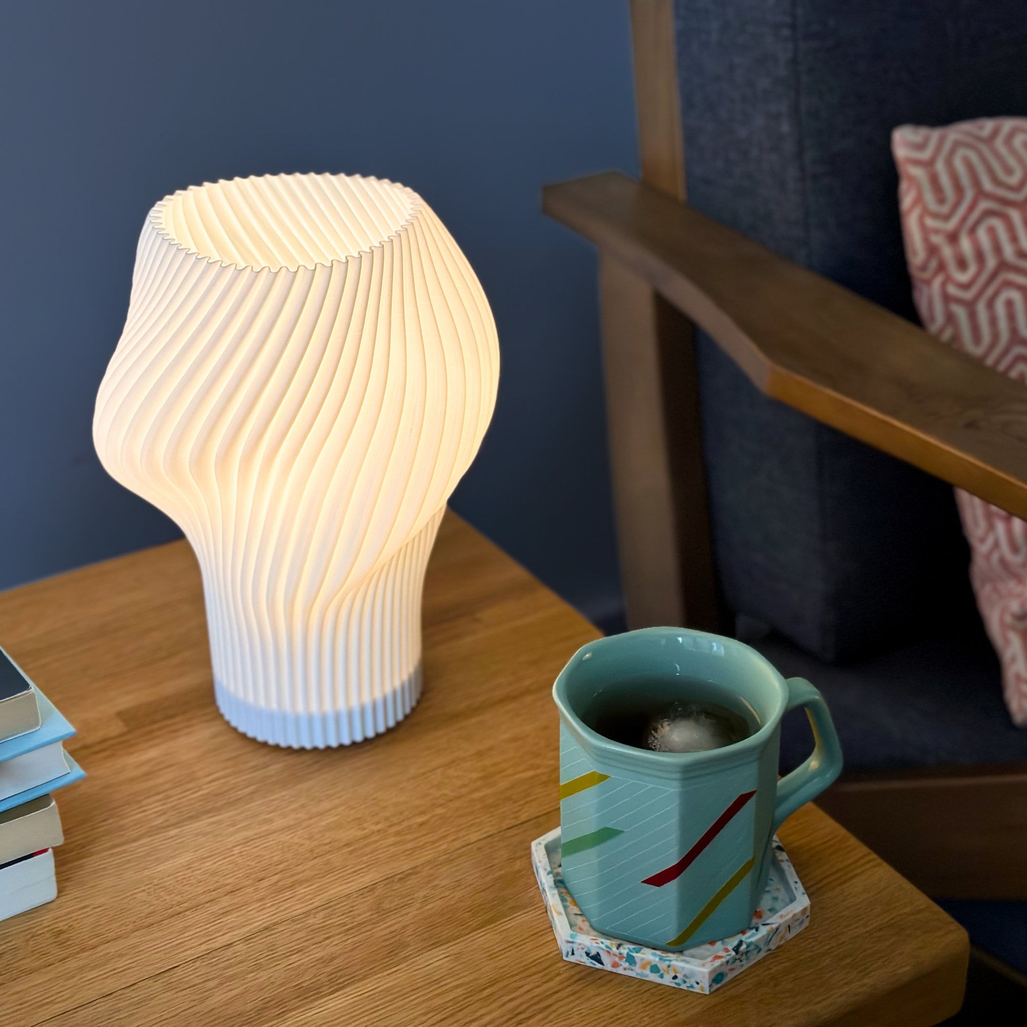 Flourish lamp illuminated on a side table with iced tea and stacked books.