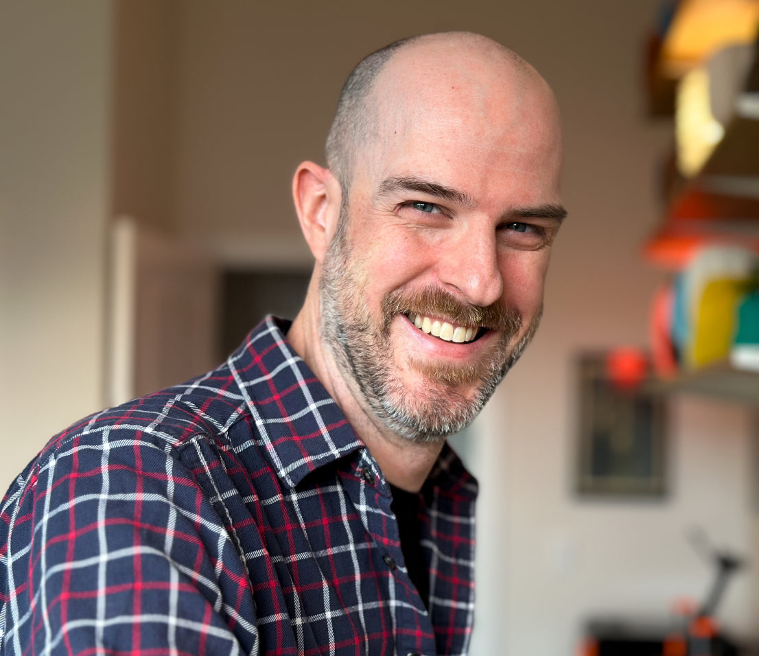 Jon May smiling with a wall of colorful lamps