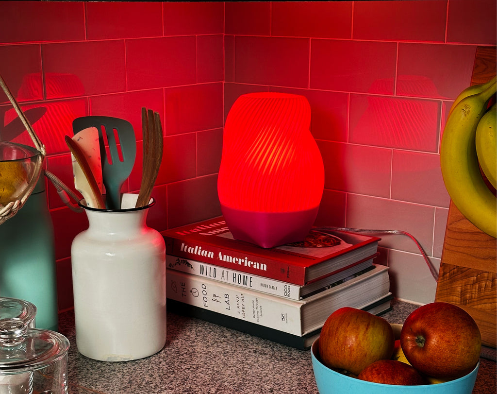 Pink Tama lamp illuminated in a kitchen, styled with stacked books, fruit and utensils