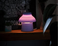 Lavender Zen Lamp illuminated on a table, styled with a poster and plants.