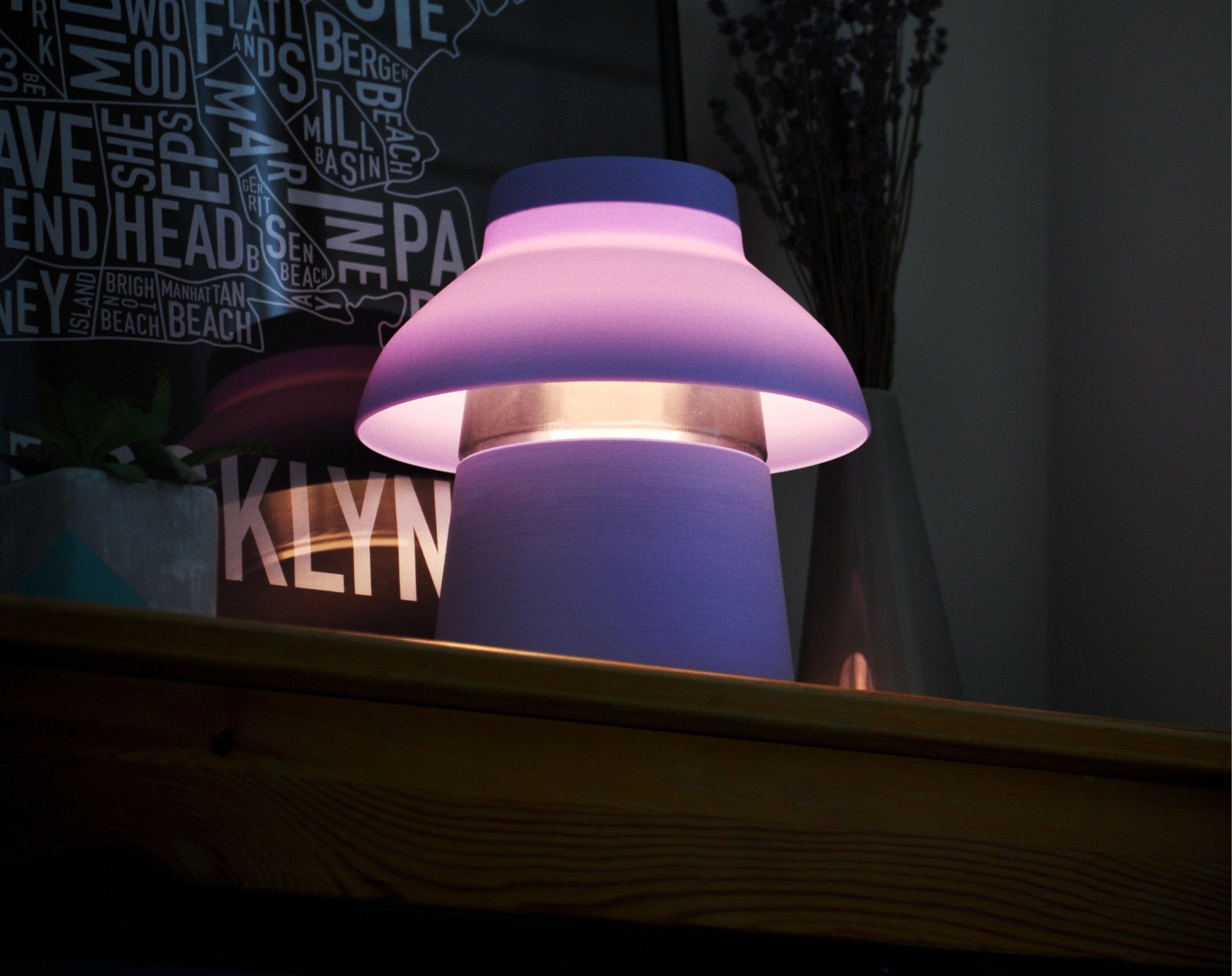 Lavender Zen Lamp illuminated on a table, styled with a poster and plants.