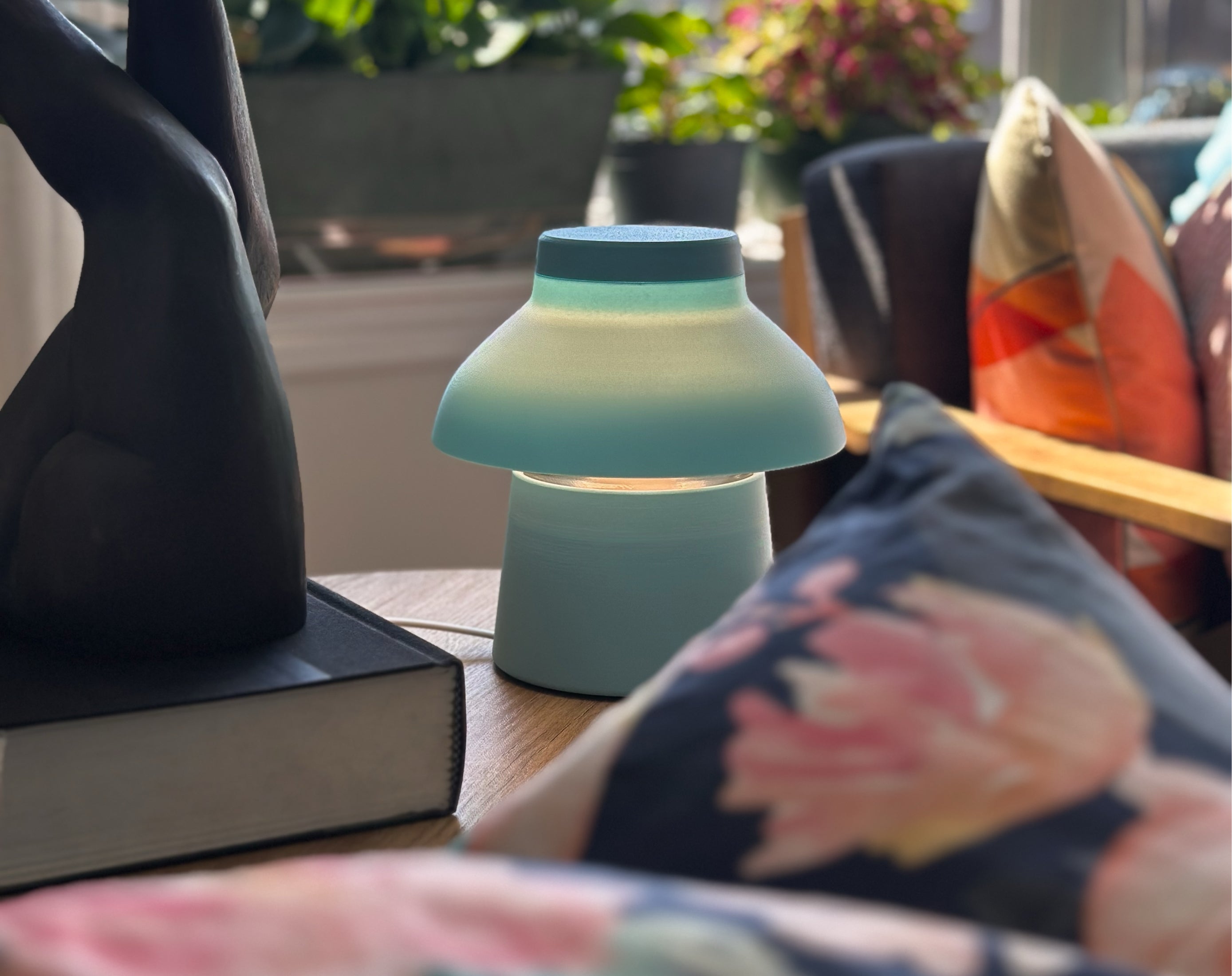 Light blue Zen Lamp illuminated on a living room table with pillows, plants, and a bronze sculpture.