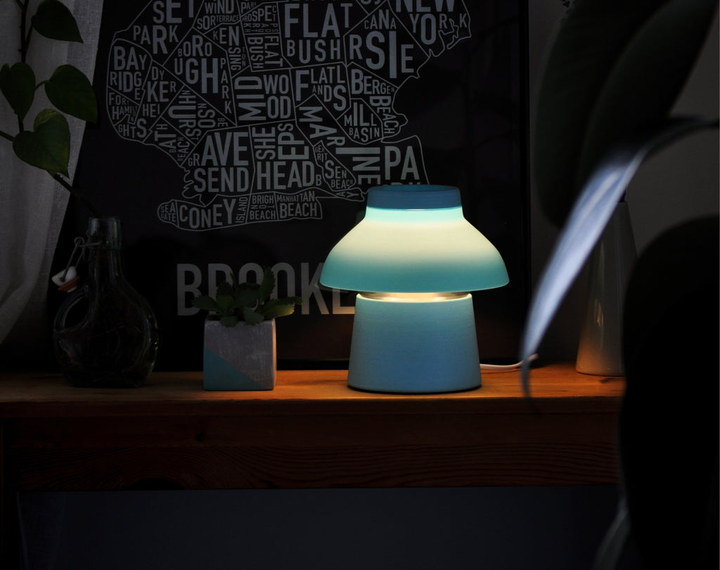 Light blue Zen Lamp illuminated on a table, styled with a poster and plants.